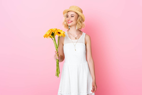 woman in straw hat and white dress holding yellow flowers on pink  - Φωτογραφία, εικόνα