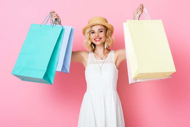 femme en chapeau de paille et robe blanche tenant des sacs à provisions sur rose  - Photo, image