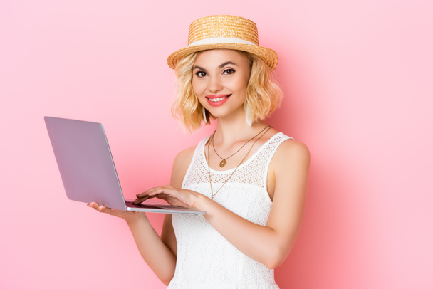 woman in straw hat using laptop on pink - Foto, Imagen