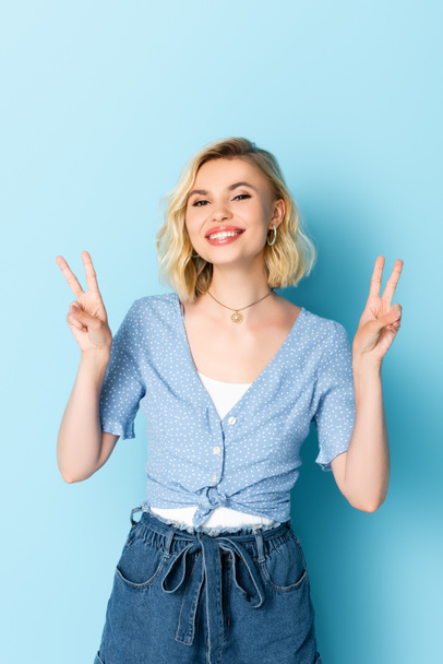 woman looking at camera while showing peace sign on blue  - Photo, Image