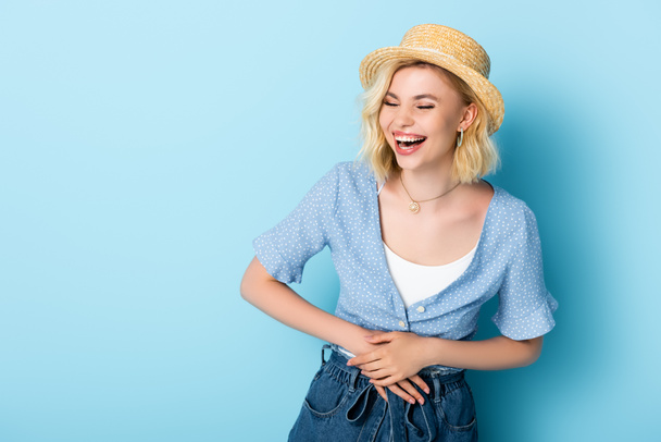 woman in straw hat laughing and touching belly on blue  - Photo, Image