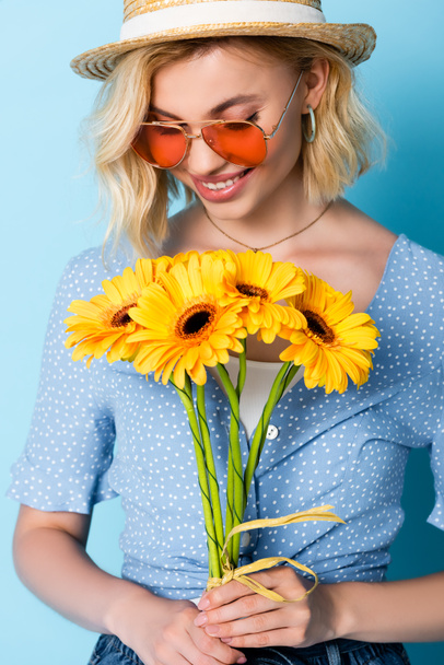 woman in straw hat and sunglasses holding flowers on blue - Foto, immagini