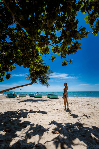 Giovane donna sexi con una palma nella spiaggia tropicale Mui Ne in Vietnam. Corazze vietnamite sullo sfondo. - Foto, immagini