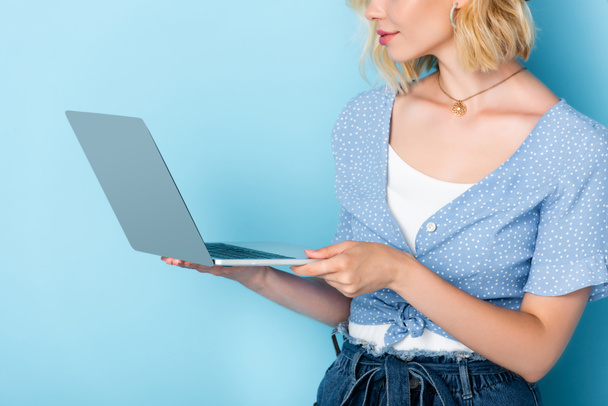 обрізаний вид молодої жінки, використовуючи ноутбук на синьому
 - Фото, зображення
