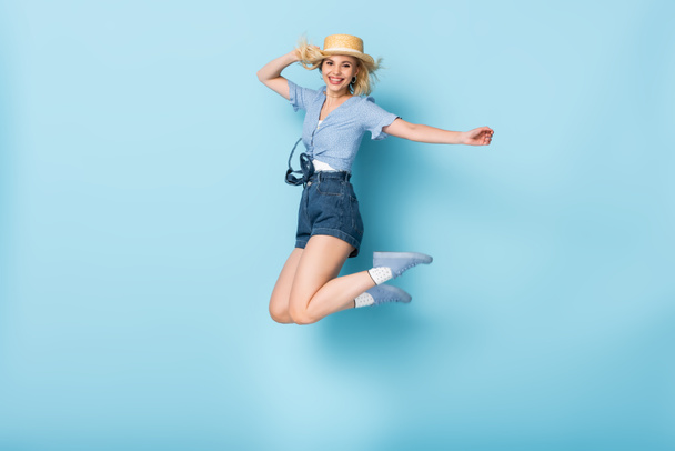 jeune femme en short et chapeau de paille sautant sur bleu - Photo, image