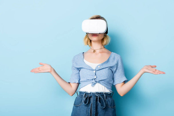 mujer joven en auriculares de realidad virtual gestos en azul - Foto, imagen
