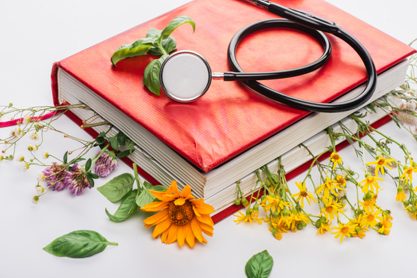 herbs in book with stethoscope on white background, naturopathy concept - Photo, Image