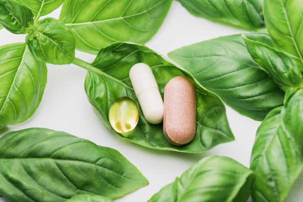 pills and green leaves on white background, naturopathy concept - Foto, Imagen