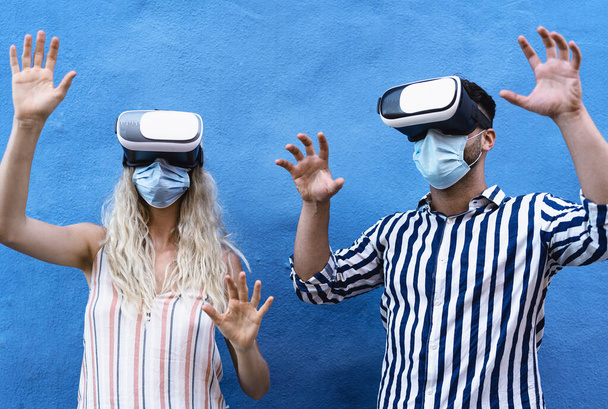 Jeune couple portant un masque chirurgical du visage s'amuser avec des lunettes de réalité virtuelle pendant l'épidémie - Les gens millénaires à l'aide novateur vr lunettes casque - génération de jeunes et concept de technologie - Photo, image