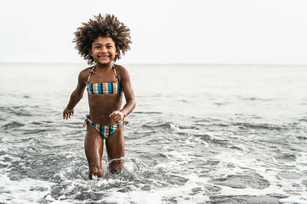 夏休み中に海の水の中で遊ぶことを楽しんでいるアフロの子供-子供と旅行の休暇のコンセプト - 写真・画像