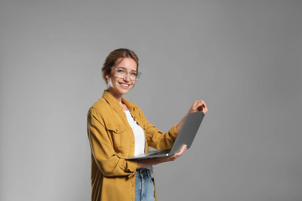 Portrait of young woman with modern laptop on grey background - Foto, Imagen