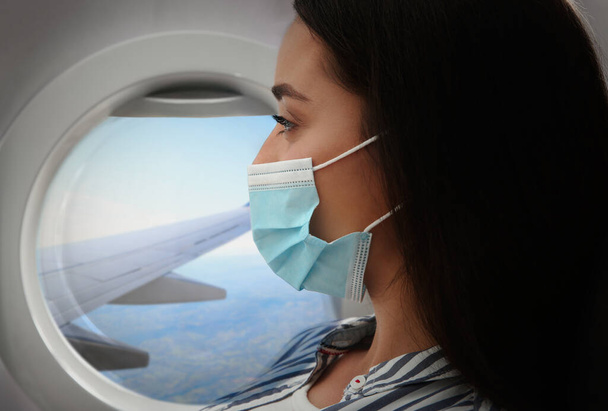 Traveling by airplane during coronavirus pandemic. Woman with face mask near porthole - Foto, Imagen