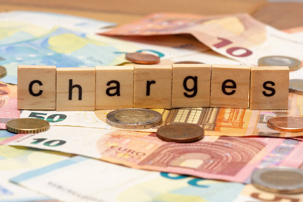 Wooden letters composing the word "charges" on a backgroud of euro banknotes and coins - Photo, Image