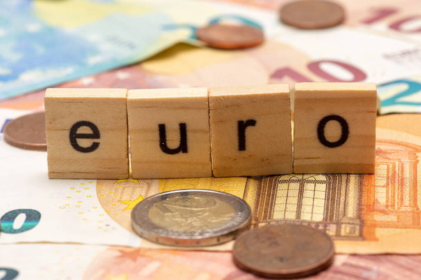 Litery drewniane zawierające słowo "euro" na tle banknotów i monet euro - Zdjęcie, obraz