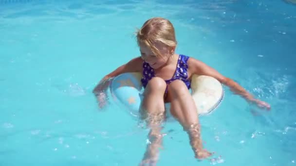 La niña está descansando en la piscina del hotel. Flota en un anillo de goma y sonríe. Nadando en un día caluroso. - Imágenes, Vídeo