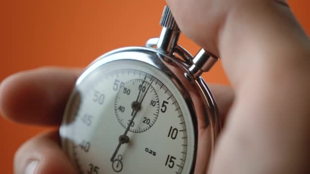 Mužská ruka drží analogové stopky na oranžovém pozadí. Čas začíná se starým chronometrem muž stiskne tlačítko start v konceptu sportu. Koncept řízení času. - Záběry, video