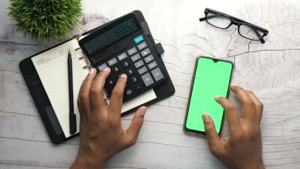 Vista superior de la mano del hombre usando el teléfono inteligente y la calculadora en la mesa  - Imágenes, Vídeo