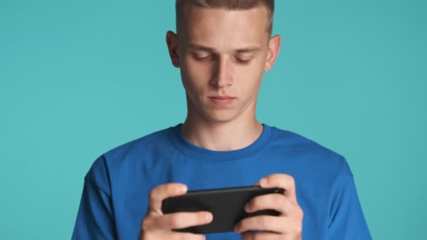 Attractive excited guy intently playing in game on smartphone over colorful background - Felvétel, videó