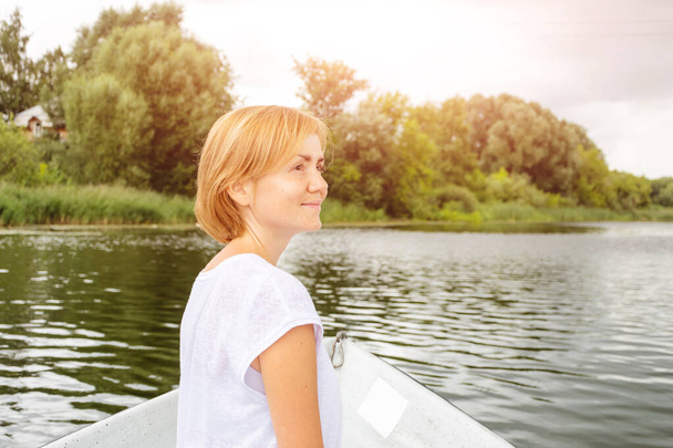 Caucasian young woman in a white T-shirt with short blond hair rides a boat. Summer vacation concept, relaxation. - Foto, Bild