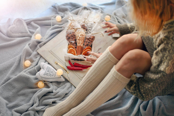 kobiece nogi w skarpetkach. Świąteczne dekoracje z lampkami. dziewczyna jest pakowanie prezenty świąteczne na koc - Zdjęcie, obraz