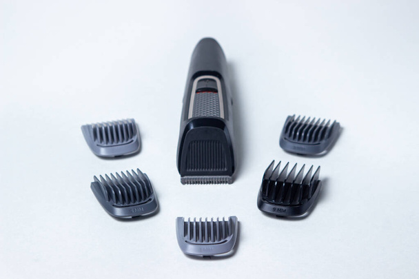 Recortadora de barba sobre fondo blanco. Los accesorios de diferentes tamaños se colocan junto a la recortadora. Cuidado de la barba. Estilo masculino - Foto, Imagen
