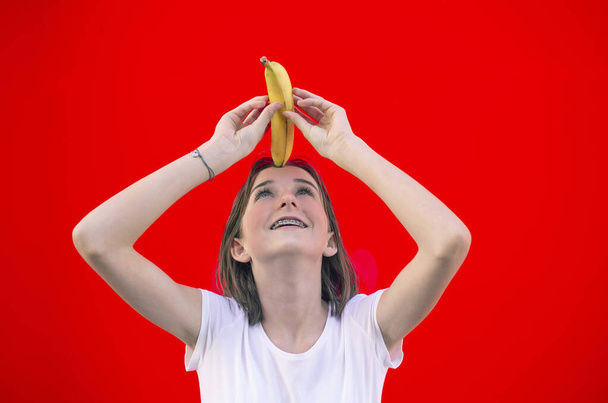 happy young girl with banana against red background - Photo, Image
