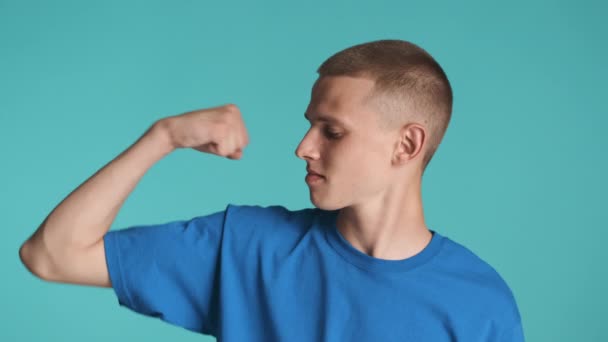 Przystojny, silny facet z pewnością pokazujący mięśnie bicepsów przed kamerą na kolorowym tle. Wyrażenie mocy - Materiał filmowy, wideo