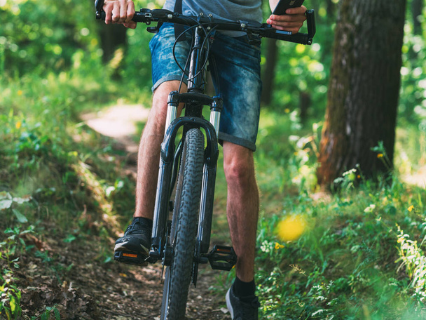 Ciclista en el bosque en una bicicleta de montaña. Ver la ruta en su teléfono - Foto, imagen