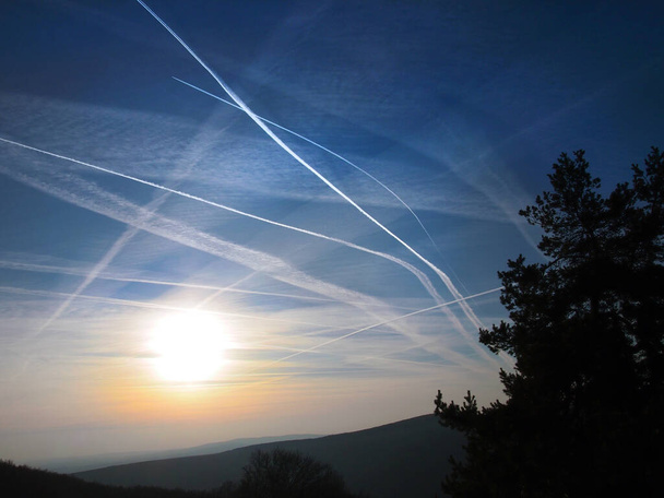 Mavi gökyüzünde ve turuncu günbatımında uçak izleri var. Birçok eski ve yeni yoğunlaşma izleri. CO2 kirliliği. - Fotoğraf, Görsel