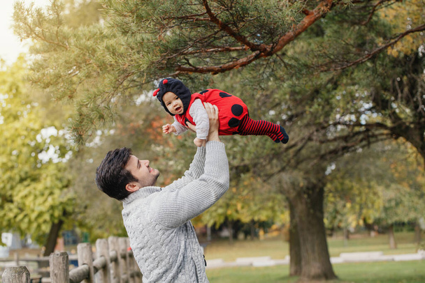 Feliz sorrindo pai caucasiano pai com bonito adorável bebê menina em traje de joaninha. Família no outono queda parque ao ar livre. Conceito sazonal de férias de Halloween
.  - Foto, Imagem
