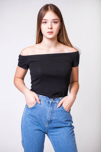 Closeup portrait of a young beautiful girl in blue jeans - isolated on gray background - 写真・画像