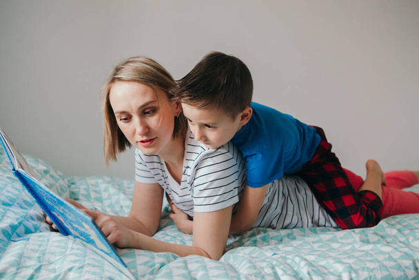 Happy Caucasian mother and son family reading book in bedroom. Mom and boy child at home spending time together. Parent talking communicate to kid. Real people authentic lifestyle. - Photo, Image