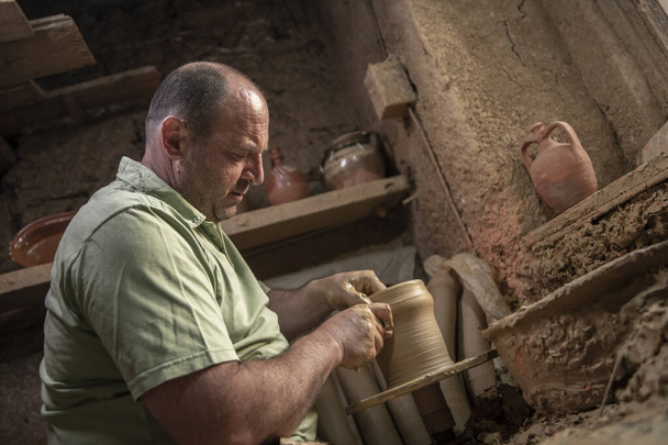 男性の陶芸家は陶器の車輪に鍋を作ります。回転ホイール上のテラコッタ陶器の男。土地の中心を持つ陶器のアイデアを作る男性 - 写真・画像
