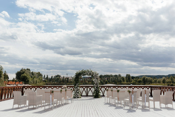Wedding ceremony place. White chairs for guests at the wedding ceremony and wedding arch. High quality photo - Photo, Image