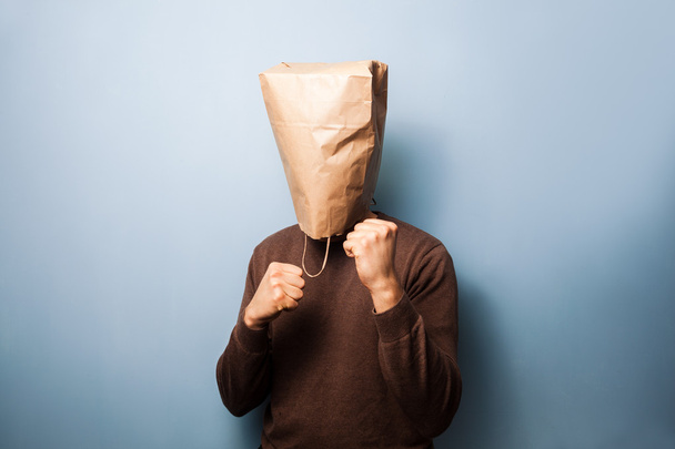 Young man with bag over his head in fighting stance - 写真・画像