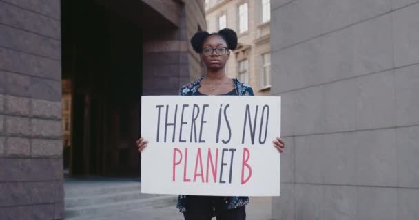 Young african american girl holding there is no planet b cardboard while standing at city street. Female acrivist supporting eco campaign. Concept of environmental protection. Zoom in. - Materiał filmowy, wideo