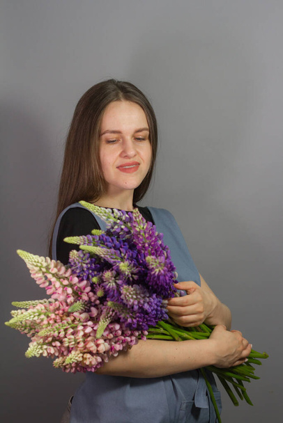 Brunette florist girl with bouquet of multi-colored lupins on grey background, woman florist with bouquet isolate, selective focus - Φωτογραφία, εικόνα