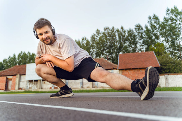 Взрослый мужчина растягивается на беговой дорожке - кавказский мужчина готовится к тренировкам на свежем воздухе - Концепция оздоровительного и фитнес-отдыха реальных людей - Фото, изображение