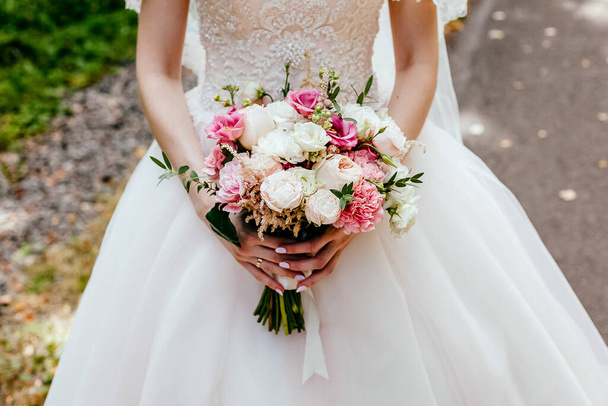 Bridal bouquet, hold the wedding bouquet in your hand, satin ribbons adorn the wedding bouquet of roses, on the background of the bride's dress, fresh flowers, made by a florist, the fragrance of flowers - Zdjęcie, obraz