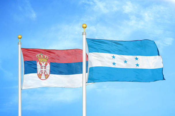 Serbia y Honduras dos banderas sobre asta de bandera y fondo azul cielo nublado - Foto, Imagen
