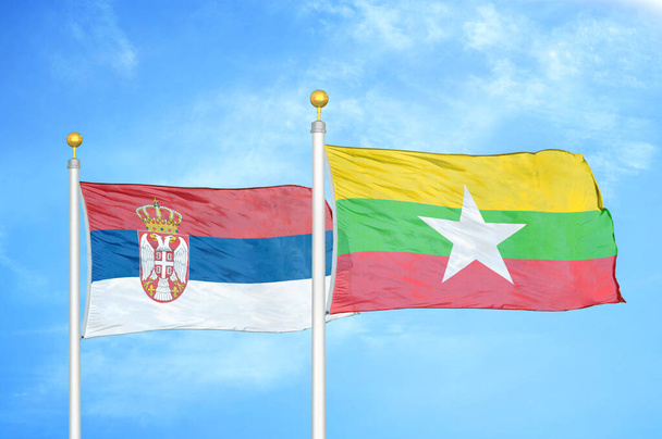 Serbia y Myanmar dos banderas sobre asta de bandera y fondo azul nublado - Foto, Imagen
