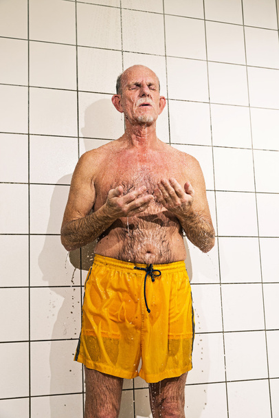 Senior man taking a shower in bathroom. Wearing yellow swimming - Foto, afbeelding