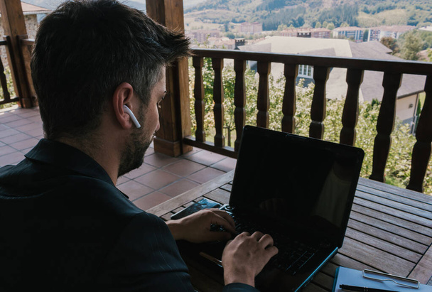 Homme d'affaires d'âge moyen travaillant à la maison à l'aide d'un ordinateur portable, écouteurs et un ordinateur portable sur la terrasse - Photo, image