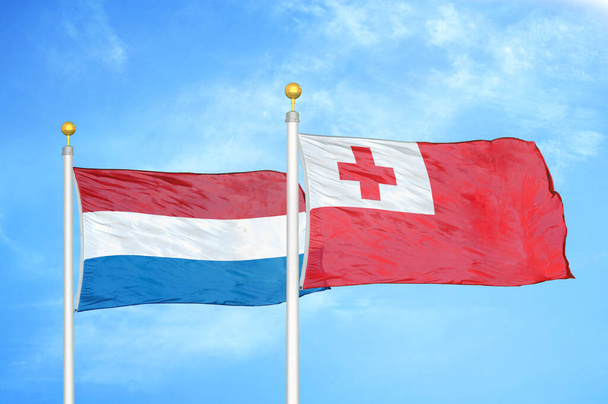 Κάτω Χώρες και Τόνγκα δύο σημαίες σε κοντάρια σημαίας και μπλε θολό φόντο του ουρανού - Φωτογραφία, εικόνα