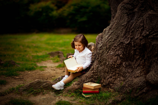 a girl in school uniform, eating a sandwich near a large tree, during a break between classes at school, September 1 - Foto, Imagen