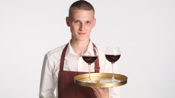Jonge knappe zelfverzekerde ober met dienblad met rode wijn gelukkig kijkend in camera geïsoleerd - Video