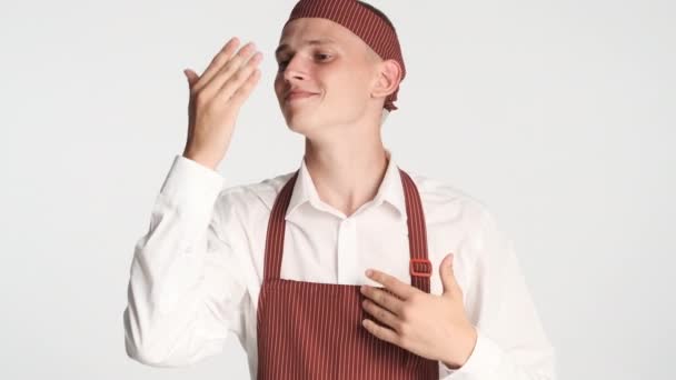 Joven guapo cocinero en uniforme felizmente oliendo delicioso olor en cámara aislada - Metraje, vídeo