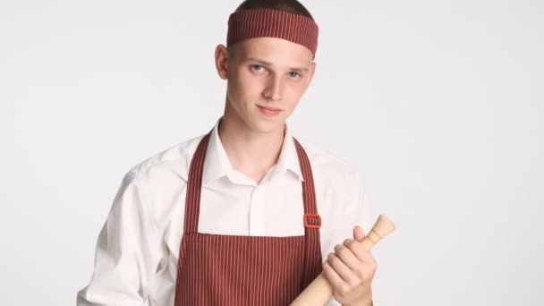 Genç, çekici aşçı üniformalı, merdaneli beyaz arka planda kameraya iyi bir jest gösteriyor. Aferin ifade. - Video, Çekim