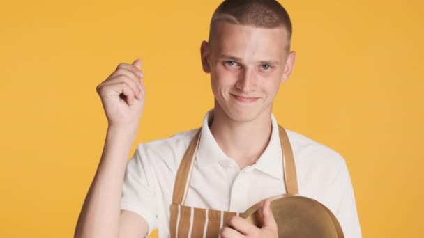 Young attractive waiter in uniform with tray confidently looking in camera showing money gesture over colorful background. Tips expression - Footage, Video
