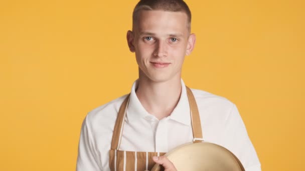 Young smiling waiter in uniform with tray happily looking in camera over colorful background - Footage, Video